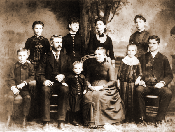 Black-and-white historical studio portrait of an extended family of ten posed together in late-1800s formal clothing