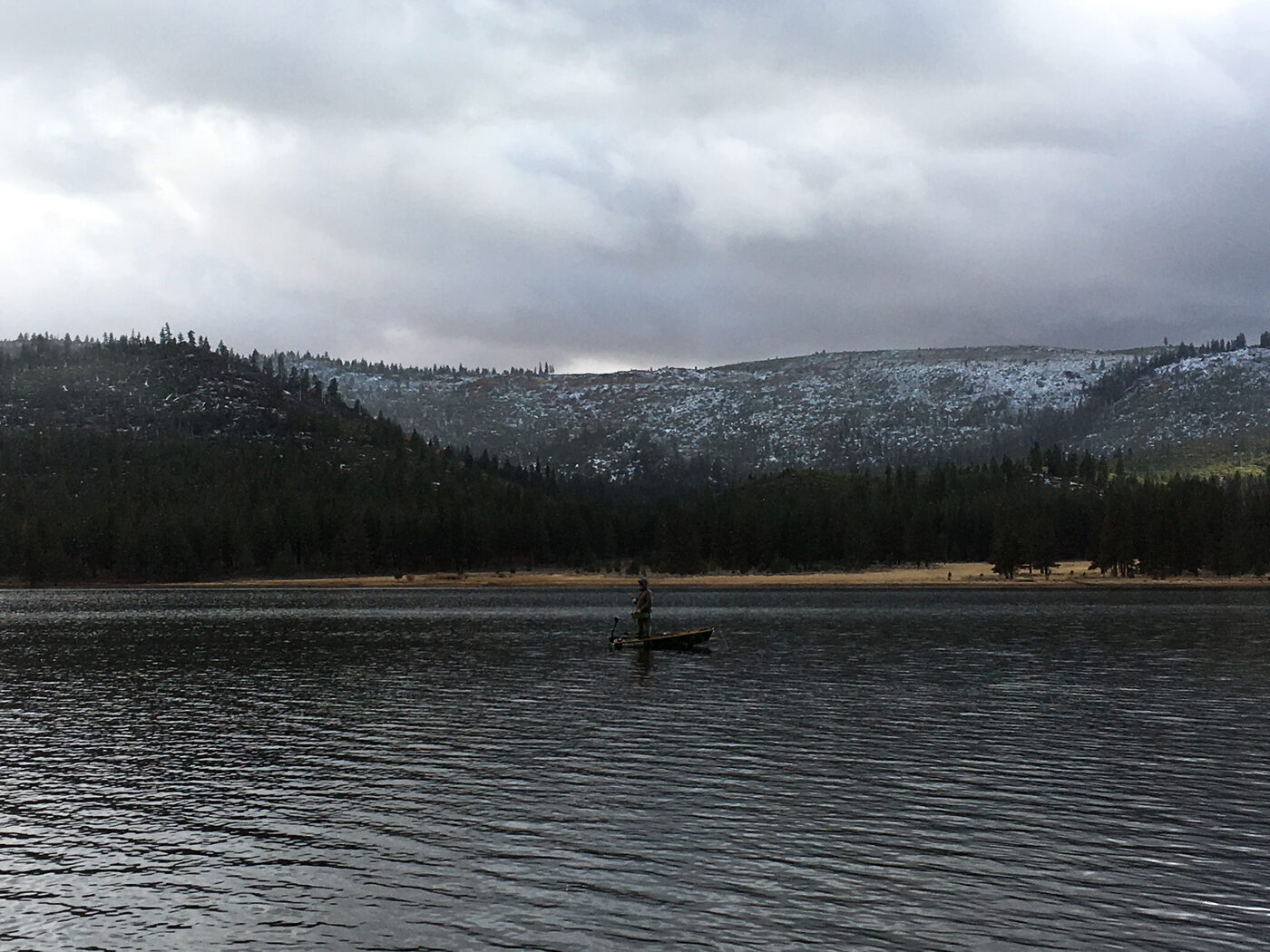 Fishing from a boat with snow-dusted hills across the water