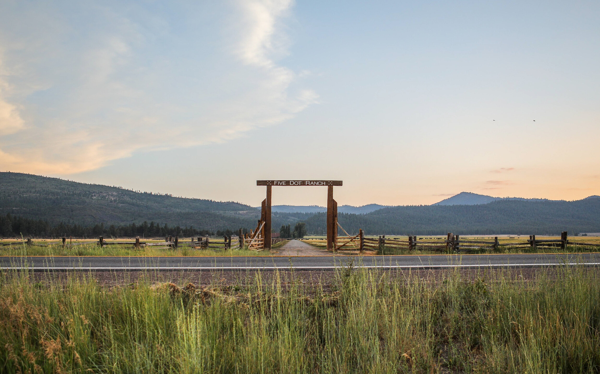 Wooden ranch entrance gate reading Five Dot Ranch at dusk, with mountains in the background