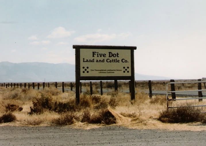 A roadside sign reading Five Dot Land and Cattle Co. along a desert highway