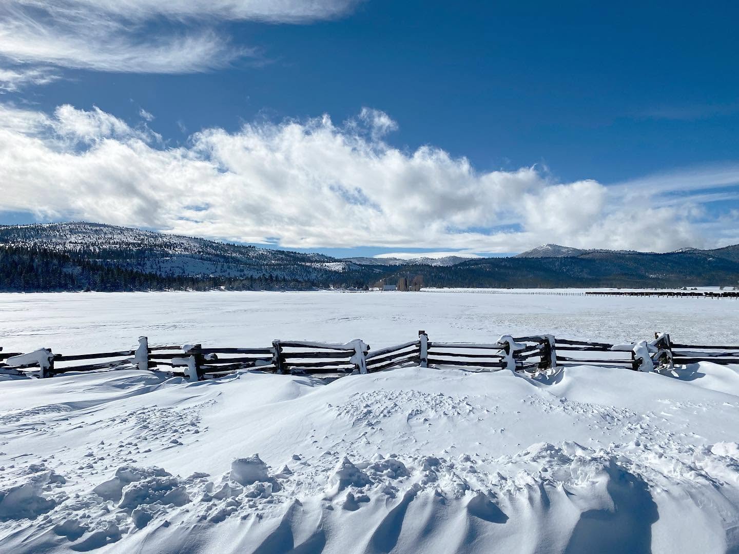 A snow-drifted split-rail fence with a frozen valley and mountains in the background