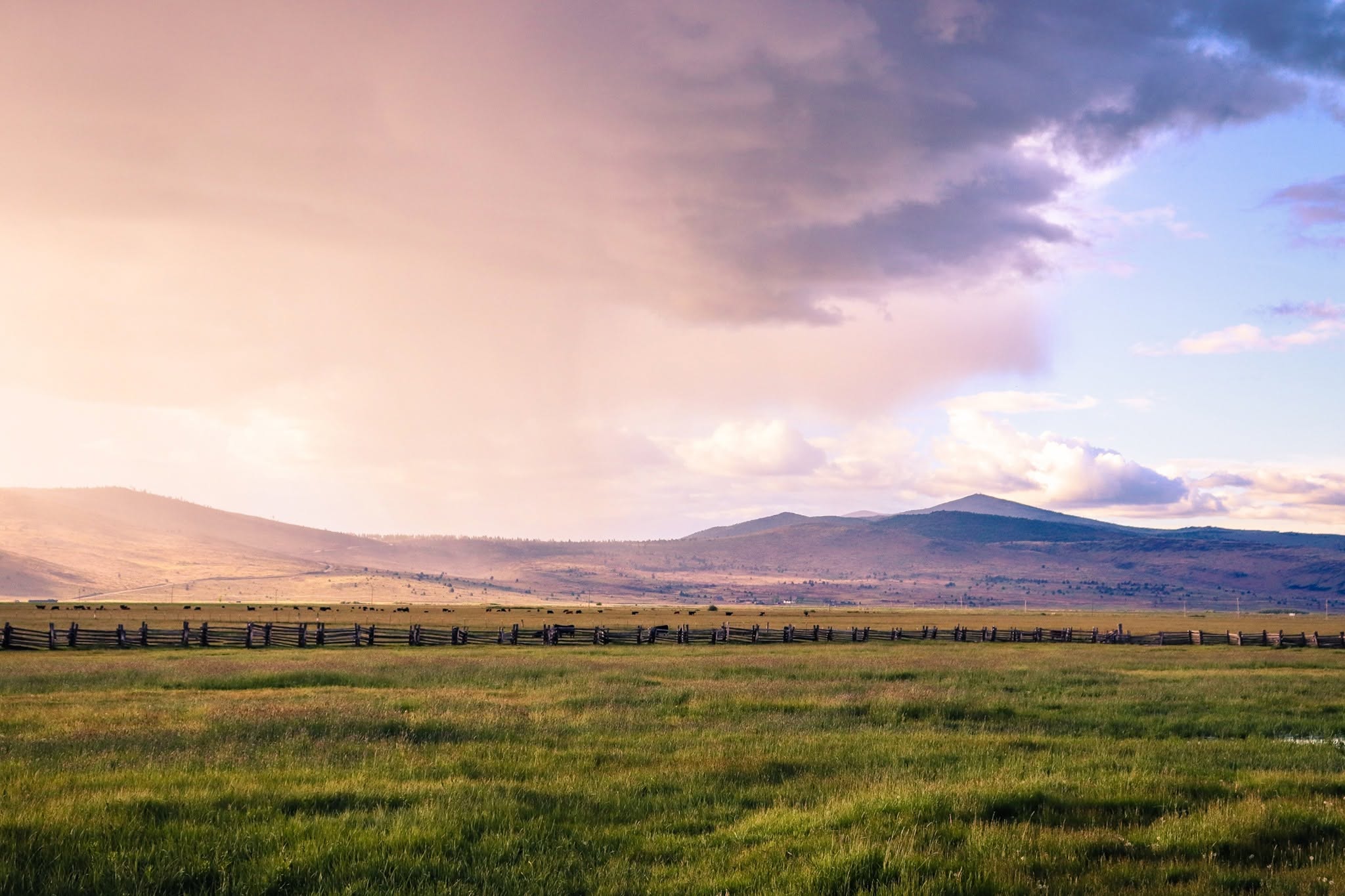 A dramatic evening sky over a ranch pasture and split-rail fence