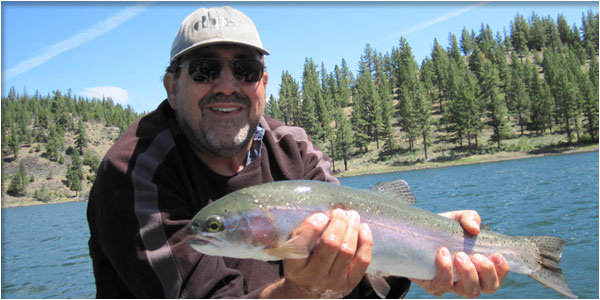 A man leaning over the side of a boat to net a trout, with another angler fishing from a float tube in the background
